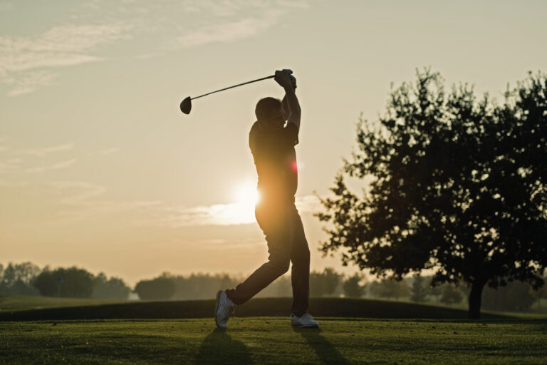 Silhouette of a golfer as he hits a perfect tee shot. Photographed against a setting sun on a course on the island of Møn in Denmark. Colour, horizontal with some copy space.